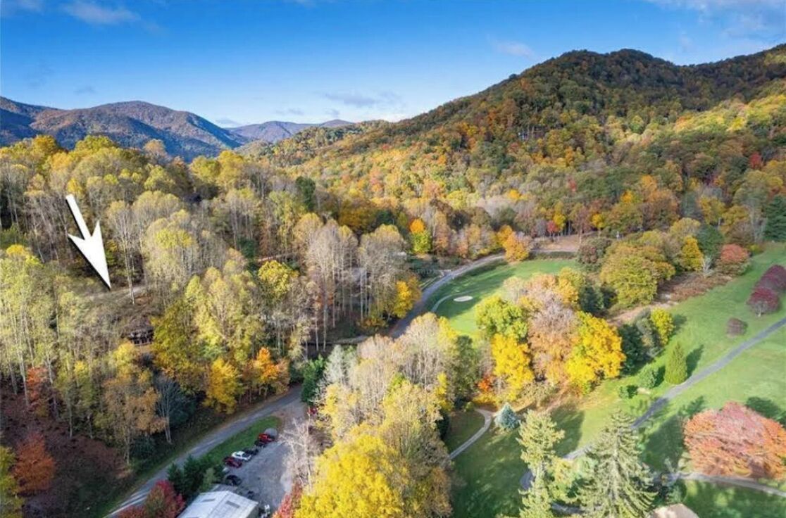 A scenic view of a mountainous area with autumn foliage, a winding road, and a parking area.