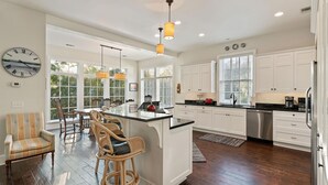 A spacious kitchen with a central island, white cabinetry, and a dining area with wicker chairs. - Shore am Happy located at the 8th Street Beach Entrance, sleeps 12 w/ large Pool (Saint Simons Island)