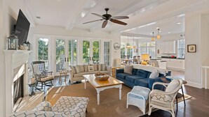 A spacious living room with a fireplace, a ceiling fan, and a view of the outdoors. - Shore am Happy located at the 8th Street Beach Entrance, sleeps 12 w/ large Pool (Saint Simons Island)