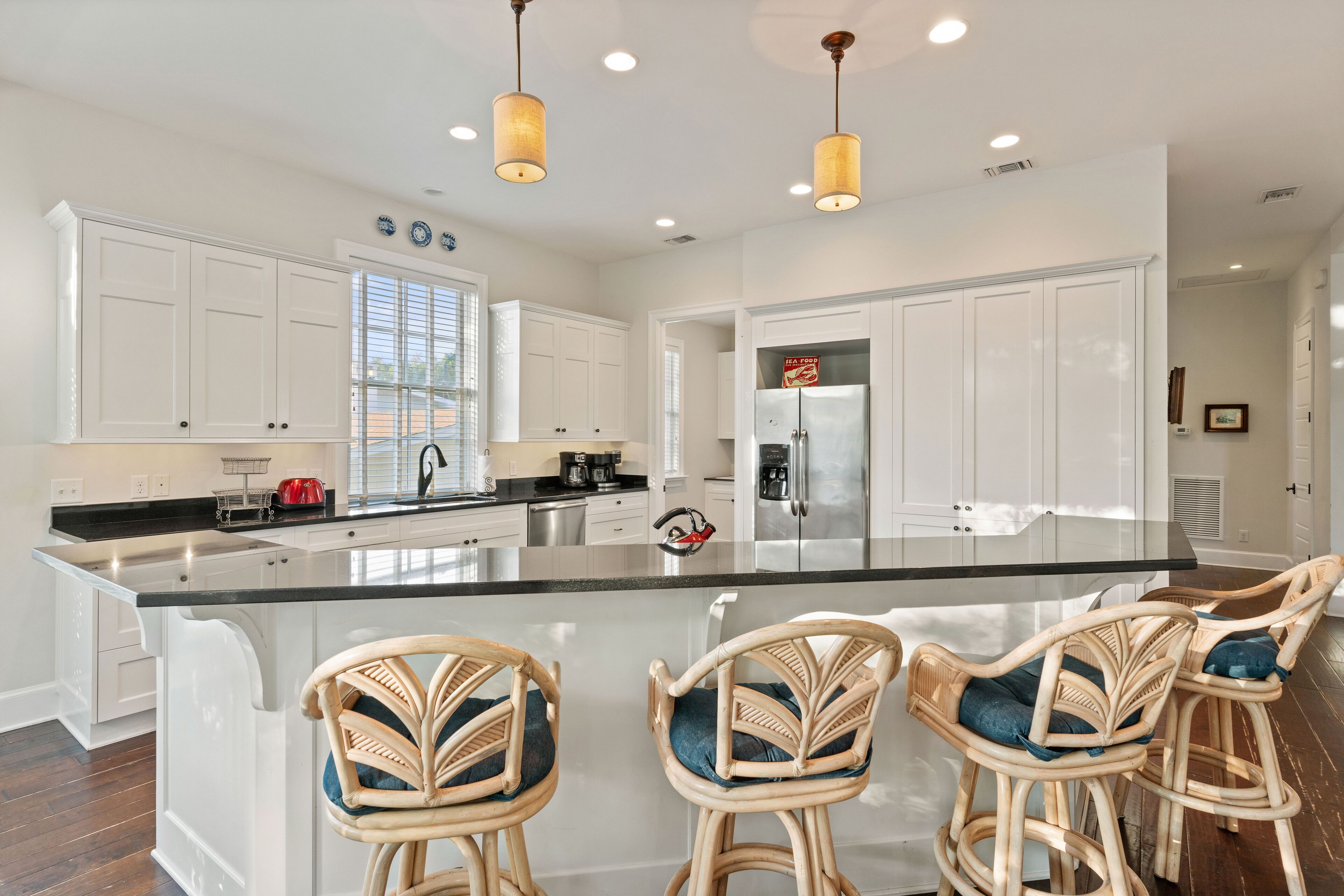 A modern kitchen with white cabinetry, a large island with bar stools, stainless steel appliances, and pendant lighting.