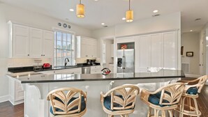 A modern kitchen with white cabinetry, a large island with bar stools, stainless steel appliances, and pendant lighting. - Shore am Happy located at the 8th Street Beach Entrance, sleeps 12 w/ large Pool (Saint Simons Island)