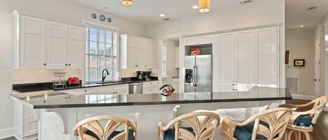 A modern kitchen with white cabinetry, a large island with bar stools, stainless steel appliances, and pendant lighting.
