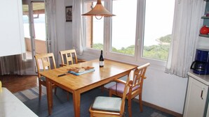 A dining area with a wooden table, chairs, a bottle of wine, and a view of greenery through large windows. - Three-flag house with a view of the Gulf of Porto-Vecchio / quiet location (Porto-Vecchio)