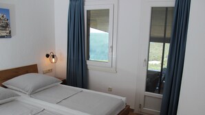 A bedroom with two beds, a nightstand with a lamp, a window with curtains, and a view of the outdoors. - Three-flag house with a view of the Gulf of Porto-Vecchio / quiet location (Porto-Vecchio)