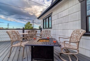 Una terraza exterior con una mesa y sillas de metal, una chimenea y vistas del cielo.