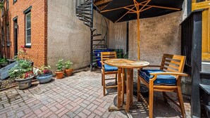 Un edificio de ladrillo con una escalera de caracol, zona de estar exterior con una mesa y sillas, y plantas en macetas.