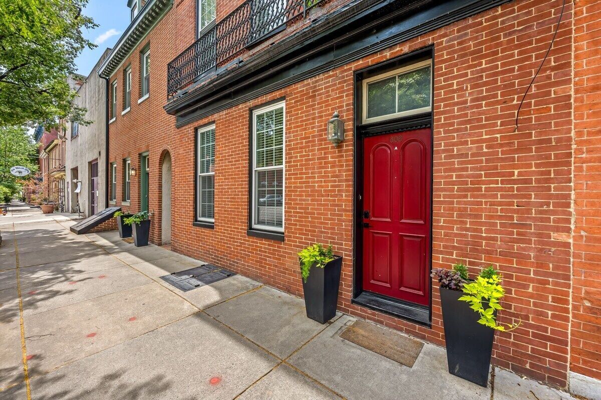 A red brick building with a red door, windows, and a black metal balcony.