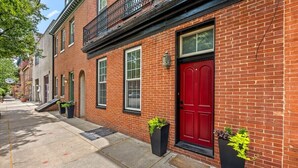 A red brick building with a red door, windows, and a black metal balcony.