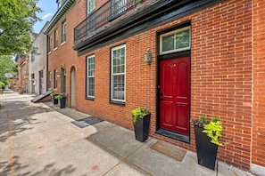 A red brick building with a red door, windows, and a black metal balcony. - Fells Point - Close to Attractions (Baltimore)