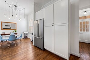 A kitchen with white cabinetry, a stainless steel refrigerator, and a dining area with blue chairs and a wooden table. - Fells Point - Close to Attractions (Baltimore)