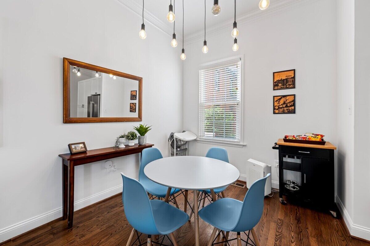 A dining area with a round table, blue chairs, a wooden console table with a mirror, and a black cart with snacks.