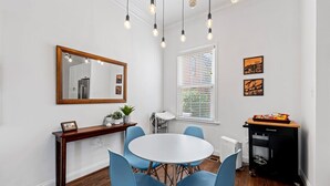 Comedor con una mesa redonda, sillas azules, una consola de madera con un espejo y un carrito negro con aperitivos.