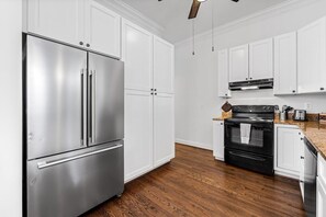 A kitchen with white cabinets, a stainless steel refrigerator, a black oven, and a wooden floor. - Fells Point - Close to Attractions (Baltimore)