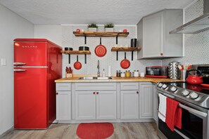 A kitchen with a red Galanz refrigerator, white cabinets, a wooden countertop, and a red kettle on the stove. - 70's Park Side Cabin with Kayaks  (Troy)