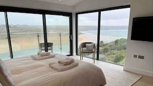 Une chambre avec un grand lit, deux fauteuils, une télévision et une vue sur la plage.