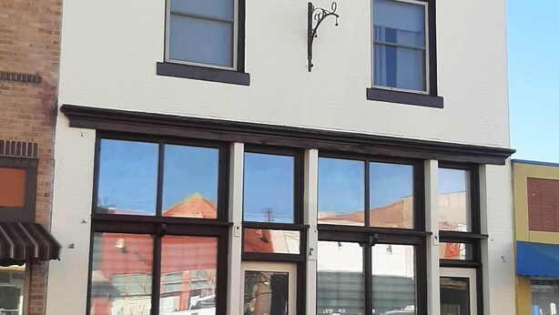 Un edificio de dos pisos con ventanas grandes y un toldo negro.