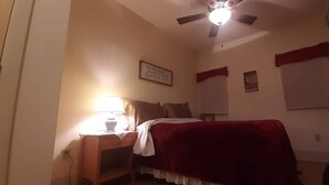 Un dormitorio con una cama, una mesita de noche con lámpara, un ventilador de techo y una pared con una cita inspiradora.