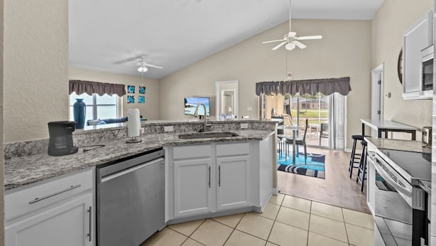 A kitchen with white cabinets, a granite countertop, a dishwasher, a ceiling fan, and a view of the backyard through a sliding glass door. - Peaceful home with Pool Dog friendly 4 Bedrooms 3 Bathrooms backyard view water. (Davenport)