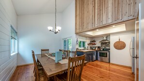 A modern kitchen with wooden cabinets, a dining area with a wooden table and chairs, and a hanging light fixture. - Cheerful, spacious family cabin ready for fun! (Shaver Lake)