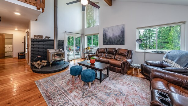 A spacious living room with a fireplace, leather furniture, and large windows offering a view of the outdoors. - Cheerful, spacious family cabin ready for fun! (Shaver Lake)