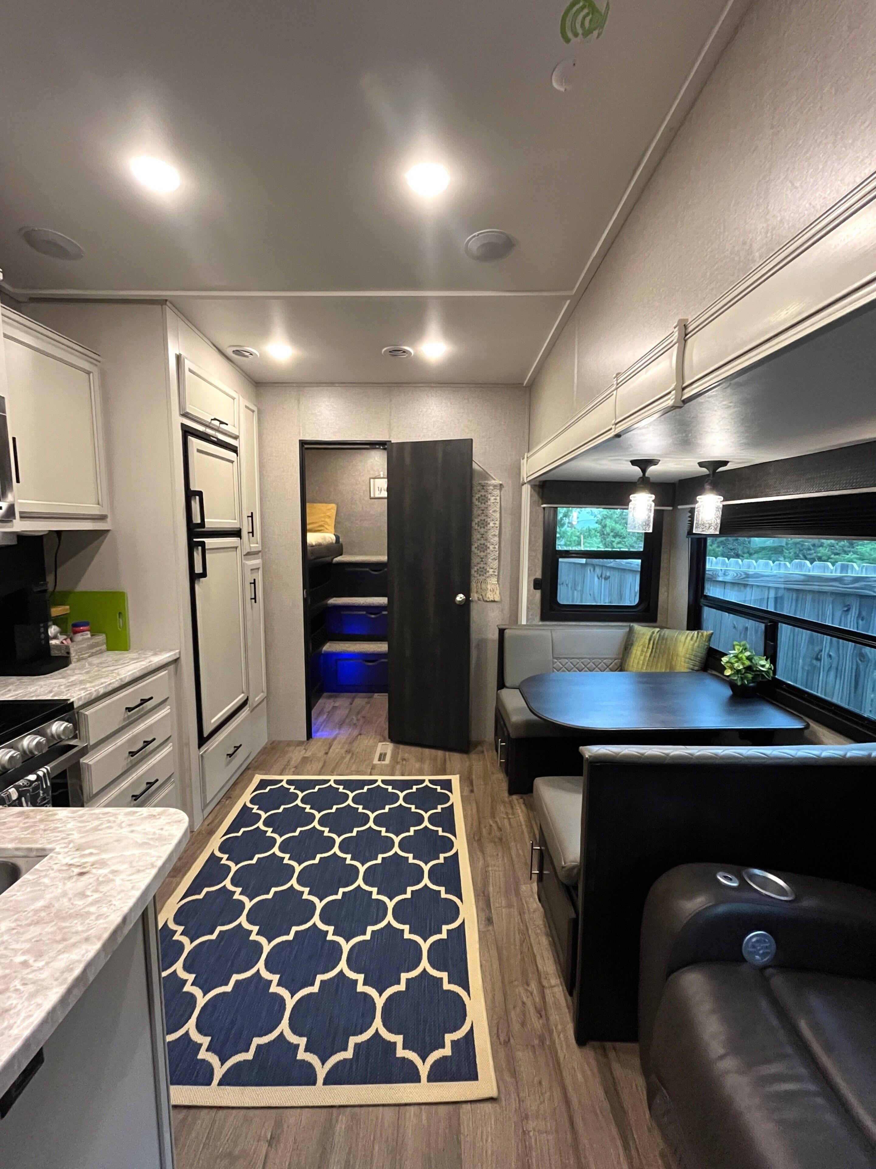 A compact RV interior with a kitchenette, seating area, and a view through a window.