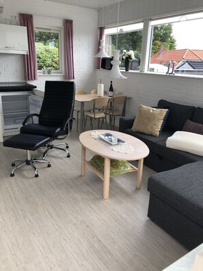 Una sala de estar moderna con una silla de escritorio negra, una mesa de centro redonda, un sofá y una mesa de comedor con sillas.
