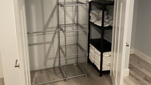 Un vestidor con una estantería metálica y un estante negro con toallas dobladas.