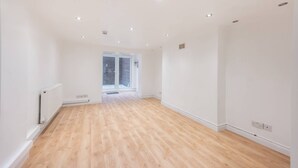 Ein geräumiges Zimmer mit Holzboden, weißen Wänden und einer Tür zum Balkon.
