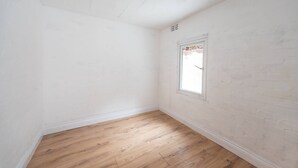 Ein Zimmer mit weißen Backsteinwänden, Holzboden und einem Fenster mit Blick auf ein Gebäude.