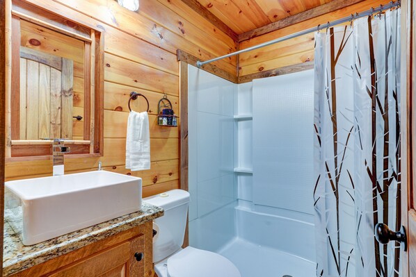 A wooden cabin bathroom with a sink, toilet, and shower.