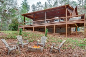 A cabin with a deck, a fire pit, and Adirondack chairs.