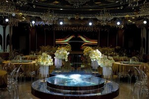 A grand ballroom with a central stage, round tables with chairs, and floral centerpieces.