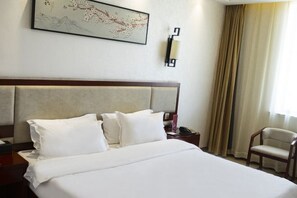 Una habitación de hotel con una cama grande, una mesita de noche, una silla y una lámpara de pared.