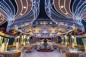 An opulent dining area with round tables, chandeliers, and a central stage. - Huaxia Hotel (Handan)