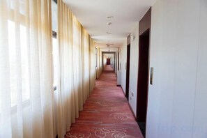 A hotel corridor with a red carpet, doors on the right, and curtains on the left. - Huaxia Hotel (Handan)