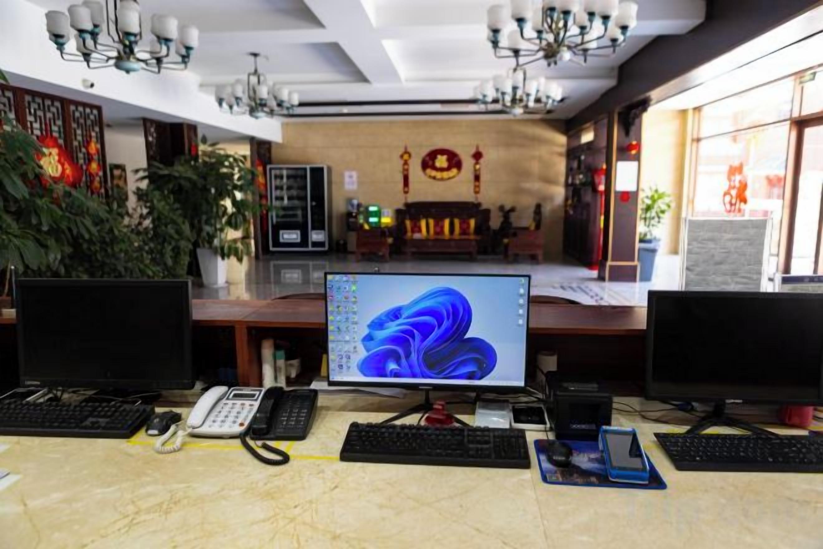 Zona de recepción de hotel con varias estaciones de trabajo de computadora, una pantalla grande mostrando una imagen abstracta azul y un altar tradicional al fondo.