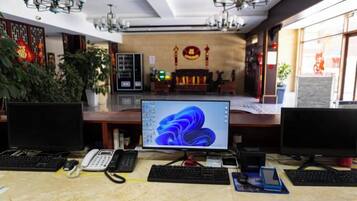 Zona de recepción de hotel con varias estaciones de trabajo de computadora, una pantalla grande mostrando una imagen abstracta azul y un altar tradicional al fondo.