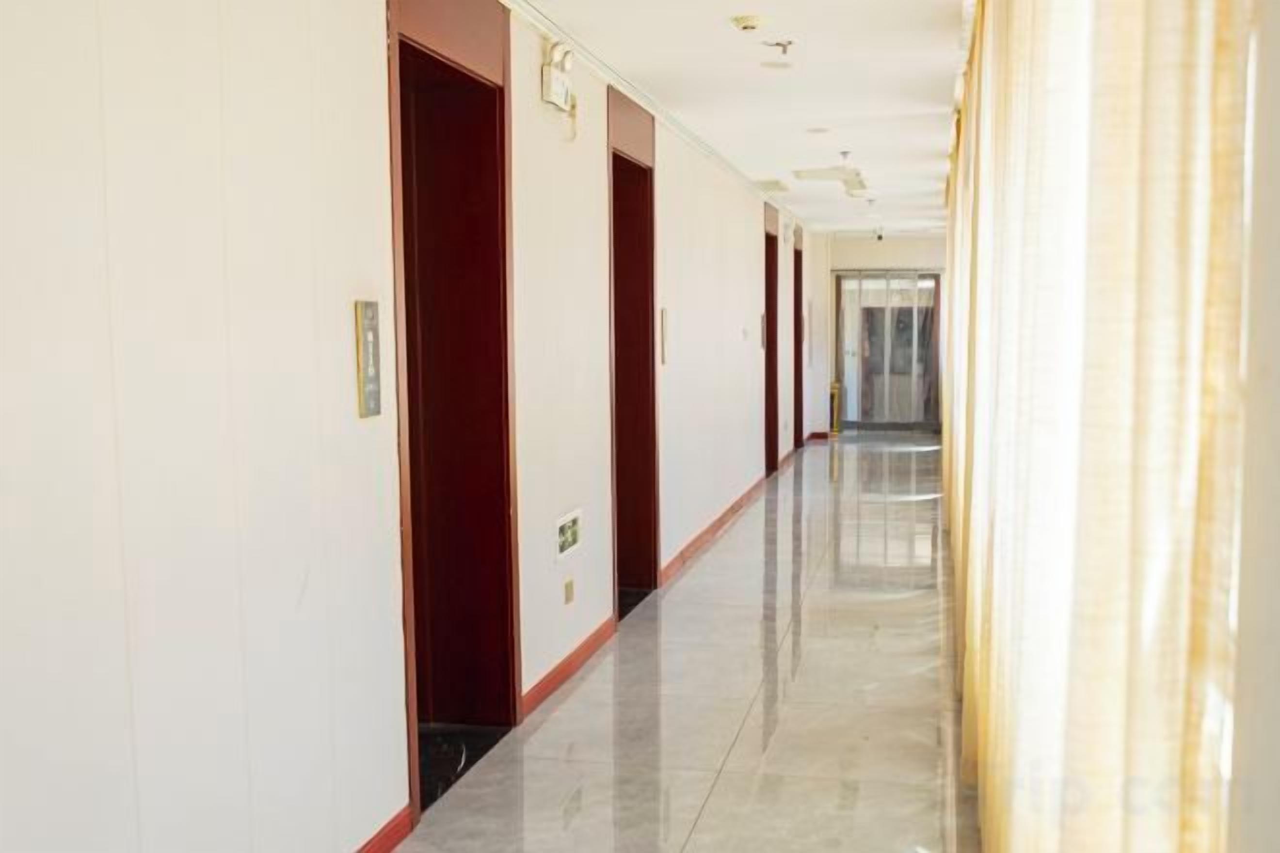 Un largo y estrecho pasillo de hotel con puertas en un lado y una pared lisa en el otro.