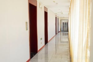 Un largo y estrecho pasillo de hotel con puertas en un lado y una pared lisa en el otro.