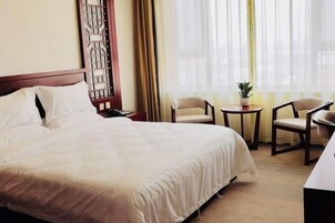 Una habitación de hotel con cama, dos sillas, una mesita con una planta y un panel decorativo en la pared.