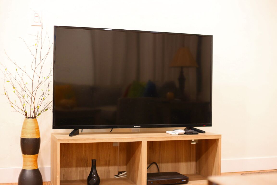 Ein Flachbildfernseher auf einem Holzständer mit einer Vase und einer Fernbedienung.