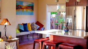 Una cucina moderna con un'isola grande, sgabelli rossi, un quadro appeso e vista su del verde all'esterno.