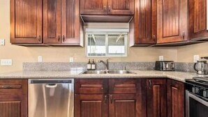 A kitchen with wooden cabinets, a stainless steel dishwasher, a sink, and a coffee maker.