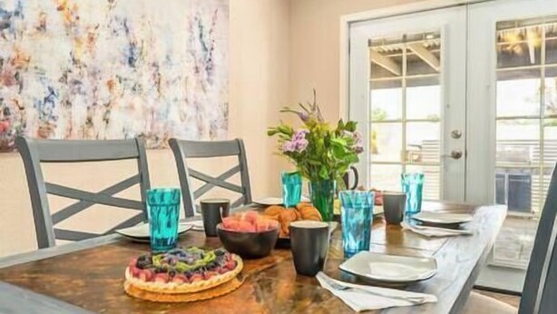 A dining table with chairs, a fruit tart, a vase with flowers, and blue cups.