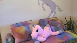 A couch with a plush unicorn toy and a wall mural of a unicorn and rainbow.