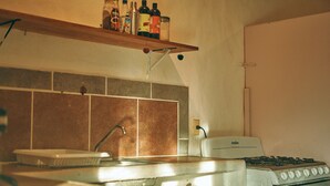A kitchen with a stove, sink, and a shelf with bottles.