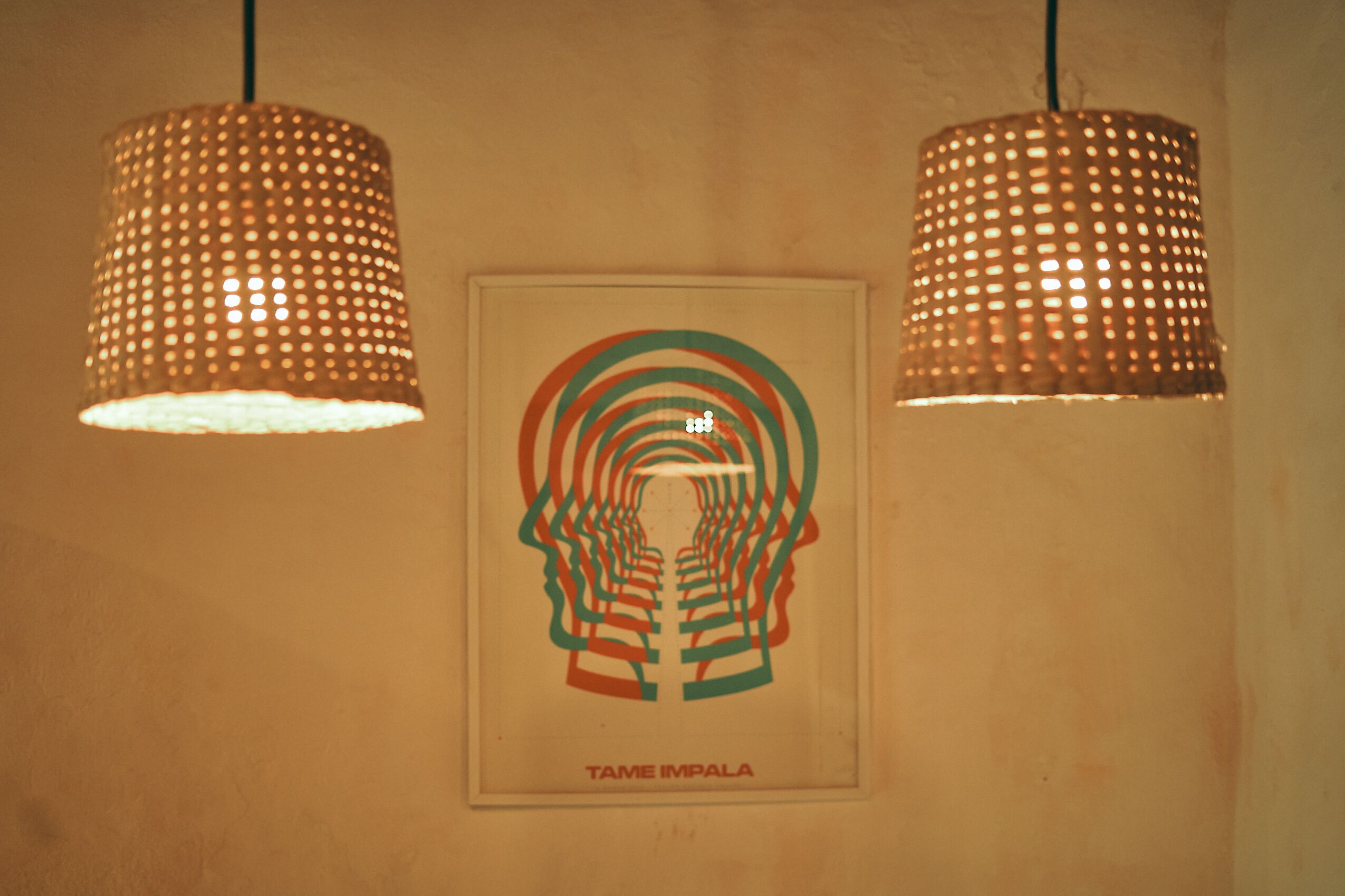Una pared con dos lámparas colgantes y una obra enmarcada que muestra el silueta de una cabeza humana y círculos concéntricos, con el texto "TAME IMPALA".