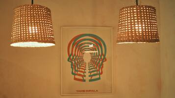Una pared con dos lámparas colgantes y una obra enmarcada que muestra el silueta de una cabeza humana y círculos concéntricos, con el texto "TAME IMPALA".