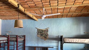 A dormitory room with bunk beds, a ceiling fan, a woven lamp, and a macrame wall hanging.