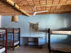 Quarto de dormitório com beliches, ventilador de teto, luminária de fibra natural e um pendente de macramé.
